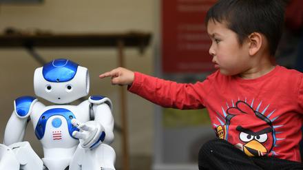Ein kleiner Junge ist im Begriff, einen sitzenden Roboter mit dem Finger anzutippen.
