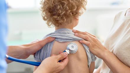 Unrecognizable male pediatrician examining curly little patient with help of stethoscope, blurred background