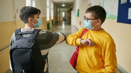 Cheerful elementary students waiting in a school hall before class starts while wearing protective face mask during COVID-19 pandemic