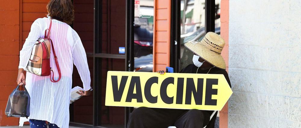 Nachlassender Impfwille in den USA: Eine Frau läuft an einem Mitarbeiter vorbei, der auf ein Impfzentrum aufmerksam macht.