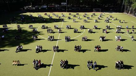In Dreiergruppen versammeln sich Berliner Abiturienten im Juni 2020 zur Zeugnisübergabe auf einem Sportplatz.