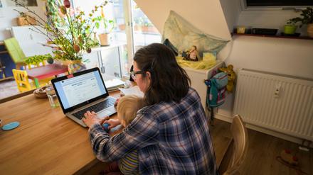 Eine alleinerziehende Mutter sitzt mit ihrem Kleinkind auf dem Schoß am Computer.