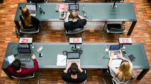 Studierende arbeiten mit ihren Laptops in einer Unibibliothek.