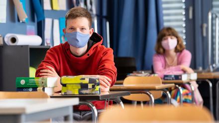 Ein Schüler und eine Schülerin sitzen in einem Klassenraum an Einzeltischen und tragen Mund-Nasen-Schutz.