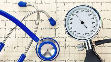 Risikofaktor Bluthochdruck. Eine Blutdruckmanschette und ein Stethoskop auf dem Ausdruck einer Herzstromkurve, einem Elektrokardiogramm (EKG).