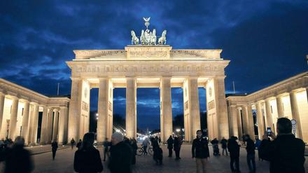 Passanten gehen im Abendlicht vor dem Brandenburger Tor in Berlin spazieren.