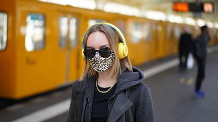 Junge Frau mit Mund-Nase-Bedeckung und Kopfhörer in einem U-Bahnhof in Berlin.