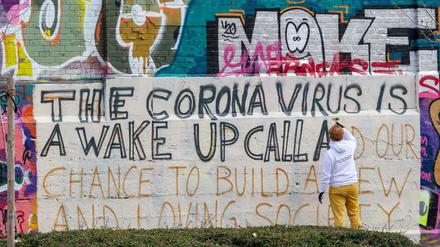 Im Münchner Schlachthofviertel schreibt ein Kunststudent ein Graffito auf eine Wand - mit dem Text: The corona virus is a wake up call and our chance to build a new and loving society.