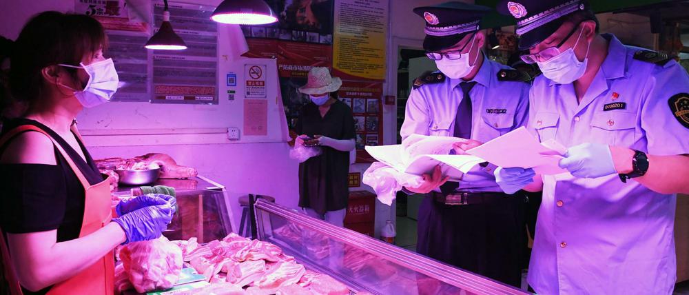 Mitarbeiter der Marktregulierungsverwaltung überprüfen an einem Marktstand in Peking die Lieferkette für Fleisch und die Einhaltung von Desinfektions-Maßnahmen, die aufgrund der Corona-Pandemie getroffen werden müssen.