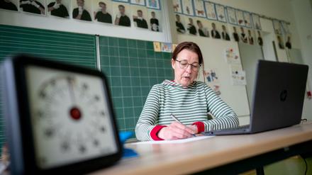 Eine Grundschullehrerin sitzt vor ihrem Laptop in einem leeren Klassenzimmer.