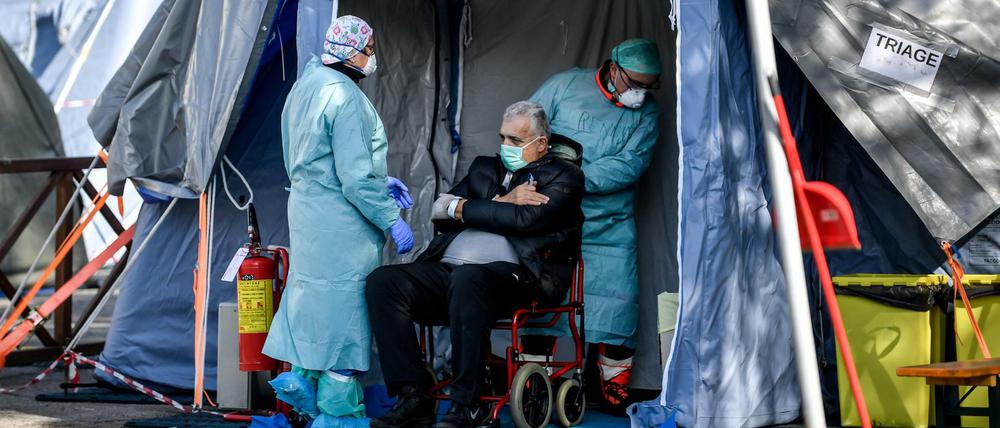 Medizinische Mitarbeiter in Schutzanzügen stehen mit einem Patienten in einem Notfallzelt in Brescia.