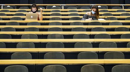 Zwei Studentinnen sitzen mit ihren Laptops in einem ansonsten leeren Hörsaal.