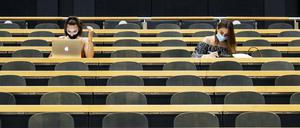 Zwei Studentinnen sitzen mit ihren Laptops in einem ansonsten leeren Hörsaal.