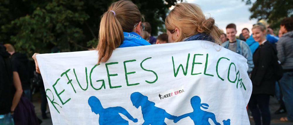 Zwei junge Frauen sind in ein Banner mit der Aufschrift Refugees welcome gehüllt.