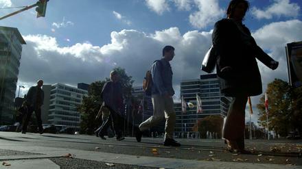 Studierende gehen im Gegenlicht auf einem Fußgängerweg vor Unigebäuden entlang.