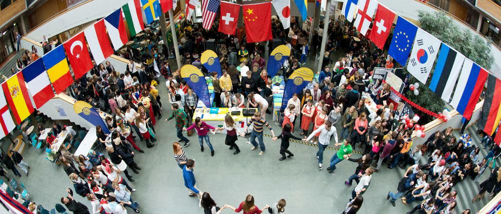 Studierende tanzen unter internationalen Flaggen in einem Hochschulauditorium.