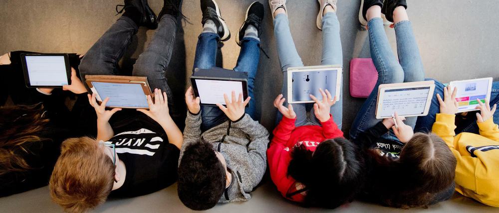 Schüler, die mit dem Rücken zur Wand sitzen, arbeiten an ihren iPads.