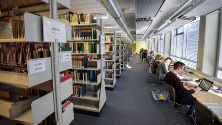 Studierende und wissenschaftliche Mitarbeiter sitzen in einer Bibliothek an ihren Laptops.