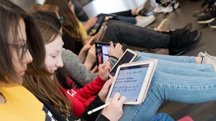 Schülerinnen sitzen mit ihren iPads auf dem Boden und lösen Matheaufgaben.