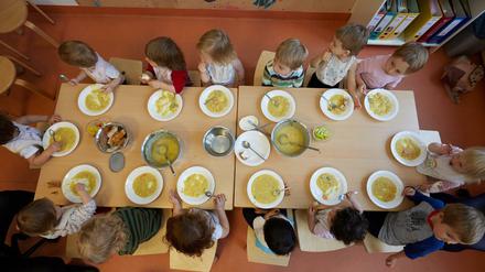 Kita-Kinder sitzen an einem Tisch und essen Suppe.