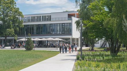 Sommerlich gekleidete Studierende und Lehrende gehen über den Campus der FU Berlin, im Hintergrund ein Mensagebäude.