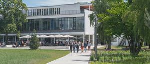 Sommerlich gekleidete Studierende und Lehrende gehen über den Campus der FU Berlin, im Hintergrund ein Mensagebäude.