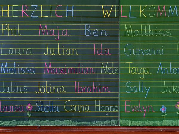 Am ersten Schultag stehen die Namen der Erstklässlerinnen - u.a. Laura, Maja, Taiga, Azra und Niclas - in bunter Kreideschrift auf einer grünen Tafel.