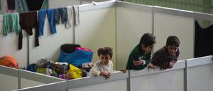 Drei Jungen schauen über eine provisorische Trennwand in einer Sammelunterkunft für Flüchtlinge.