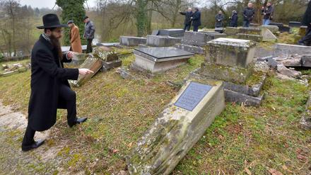 Ein Rabbiner zeigt auf einem jüdischen Friedhof auf einen umgekippten Grabstein.