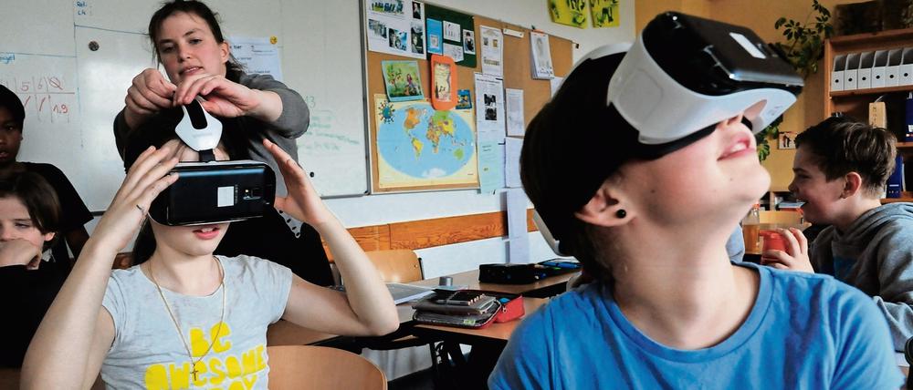 Grundschüler sitzen in einem Klassenraum, zwei von ihnen gucken durch Virtuell-Reality-Brillen.