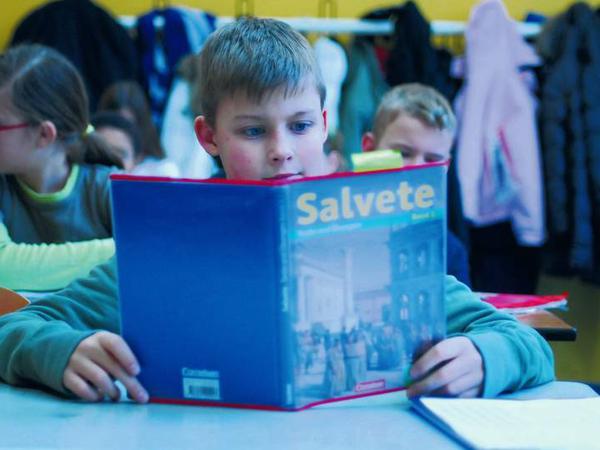 Ein Schüler sitzt im Klassenraum und liest in seinem Lateilbuch mit dem Titel "Salvete".