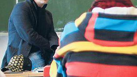 Ein Lehrer sitzt vor einer beschriebenen Tafel und spricht zu seinen Schülern.