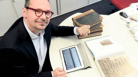 Markus Hilgert sitzt vor seinem Tablettcomputer und hält eine antike Tontafel in der Hand.