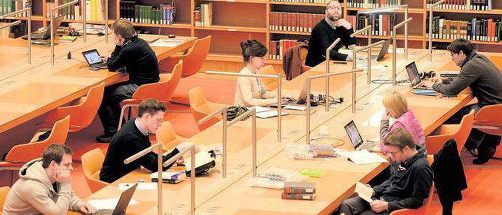 Studenten und Nachwuchswissenschaftler sitzen in der Bibliothek und arbeiten an ihren Laptops.