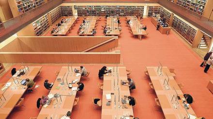 Im Lesesaal einer wissenschaftlichen Bibliothek sitzen Menschen an Tischen und lesen oder schreiben an Computern.