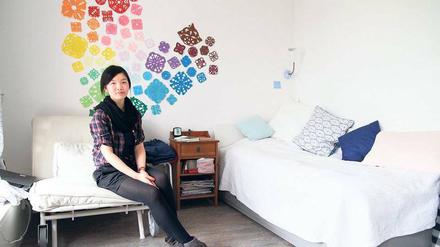 Eine Studentin sitzt in ihrem Wohnheim auf dem Sessel vor einer bunt dekorierten Wand.