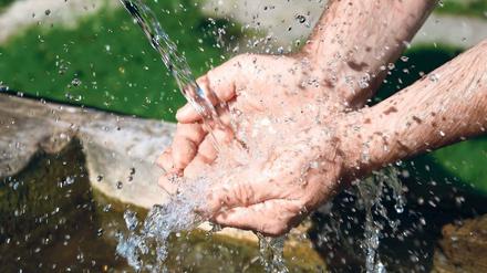 Eine Person fängt mit beiden Händen Wasser auf, das aus einer Quelle sprudelt.