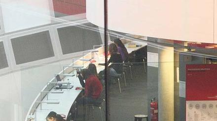 Studierende sitzen in einer Bibliothek an Tischen und arbeiten.