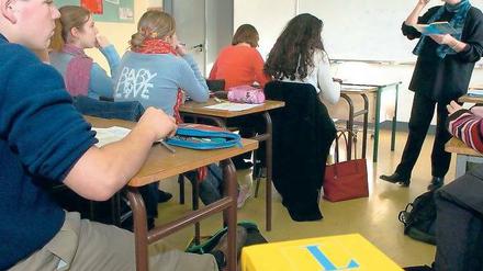 Schüler und Schülerinnen sitzen im Klassenraum, vor ihnen steht eine Lehrerin.