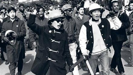 Schwarze und asiatische Studierende, die teilweise ihre geballten Fäuste erhoben haben, marschieren über den Campus einer Universität.