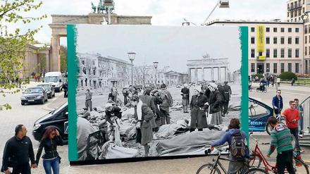 Auf dem Pariser Platz vor dem Brandenburger Tor betrachten Menschen ein Plakat, dass den Platz im Frühjahr 1945 zeigt.