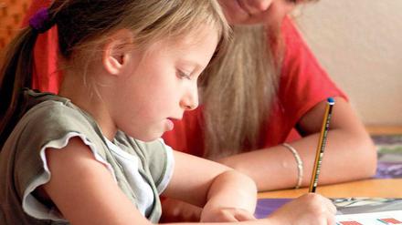Ein Kind im Grundschulalter sitzt vor Mathe-Aufgaben, eine Frau schaut ihm dabei zu.