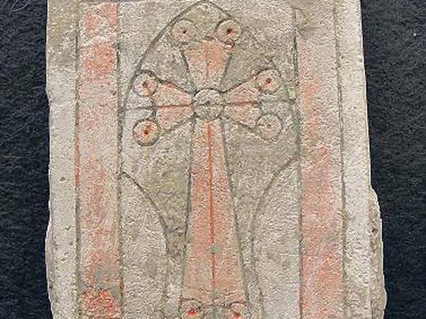 Auf einer Steinplatte ist ein Kreuz eingeritzt, das Kreuz und Teile der Umrahmung sind rot eingefärbt.