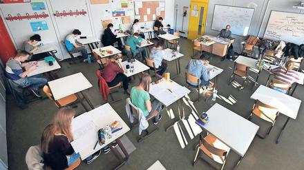Schüler sitzen in einem Klassenraum an Einzeltischen vor Aufgabenblättern.