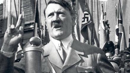 Adolf Hitler steht vor einem Mikrofon und spricht.