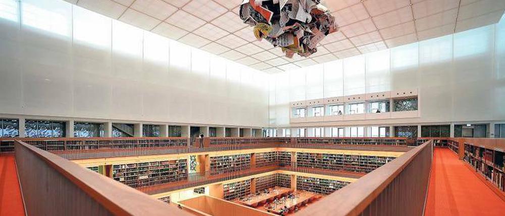 Über einem modernen Bibliotheksraum schwebt ein Kunstwerk, das an zusammengeknülltes Papier erinnert.