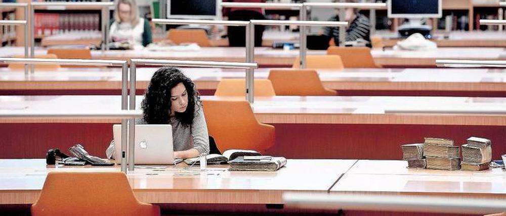 Eine junge Frau sitzt in einer Bibliothek und arbeitet am Laptop.