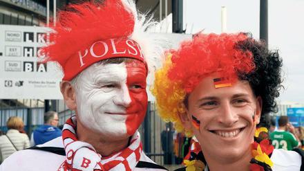 Zwei Männer, einer in den polnischen Farben geschminkt, einer in den deutschen, blicken lachend in die Kamera.