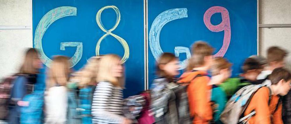Schulkinder laufen vor einer Wandtafel von links nach rechts, auf der G8 und G9 geschrieben steht.