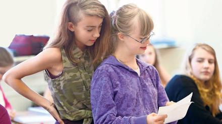 Zwei Schülerinnen stehen in einer Schulklasse und lesen gemeinsam von einem Zettel ab.